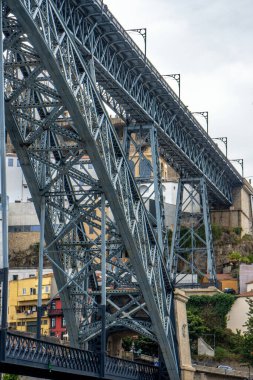 Porto 'daki Don Luis I çelik köprüsünün alçak açılı görüntüsü ve insanlar üst platformdaki Douro Nehri' nin eski mahalledeki evlerinin fotoğraflarını çekip yürüyorlar..