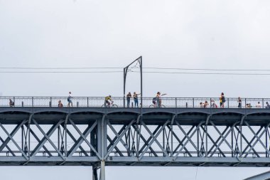 Porto 'daki Don Luis Çelik Köprüsü' nde arka planda yağmur bulutları ve insanların yürüdüğü, bisiklete bindiği ve üst platformdaki Douro Nehri 'nin fotoğraflarını çektiği bir köprü..