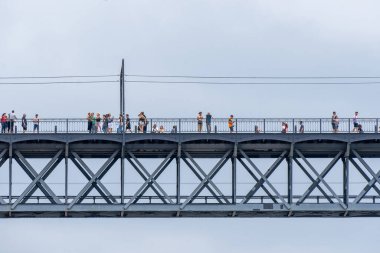 Turistler yürüyor, fotoğraf çekiyor ve Porto 'daki Don Luis Çelik Köprüsü' nün korkuluklarına yaslanıyor. Arka planda Douro Nehri 'ni görmek için yağmur bulutları var..
