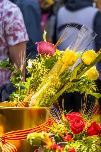 Sarı ve kırmızı güller, Katalonya bayrağının bir yayıyla altın bir çömlekte geleneksel Katalonya Festivali 'nin çiçek standında Sant Jordi' nin gününde bir çok insanın yürüdüğü yerde..