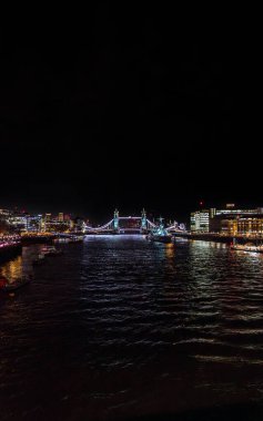 Arka planda aydınlık Tower Bridge ile Thames Nehri 'nin gece görüşü ve HMS Belfast gemisi nehirde demirledi. Binaların ve restoranların ışıkları suya yansıdı..