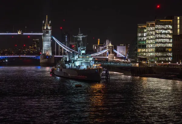 Savaş müzesi gemisi HMS Belfast, Thames Nehri 'ne kenetlenmişti. Gece aydınlanan Tower Köprüsü' nün önündeki suda bulunan restoran ve binaların ışıklarının yansımaları vardı..