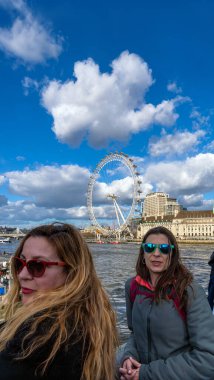 Rüzgâr ve güneş gözlükleriyle saçlarıyla poz veren mutlu ve gülümseyen lezbiyen bir çift Thames nehrinde bir feribottan kameraya bakıyor..