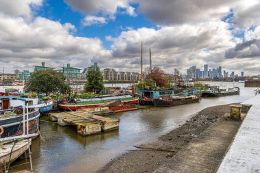 Recreational boats moored on the bank of the River Thames at Butler's Wharf in London, England, United Kingdom with the skyline and apartments in the background on the other side of the river bank. clipart