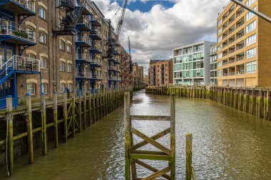 Old historic warehouse now converted into housing bordering the River Thames with green mud and moss from low tide in the Docklands area of London, England clipart