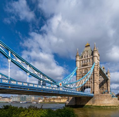 Londra 'nın Tower Köprüsü' nün Thames nehrinin kenarından beyaz bulutlar ve nehir üzerinde feribot trafiği ve arka planda rıhtımlar bulunan mavi gökyüzünün altında sabah güneşiyle aydınlatılan görüntüyü al. Birleşik Kin