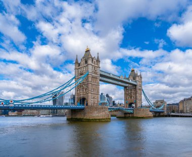 Thames Nehri 'nden Londra Kule Köprüsü' nün panoramik manzarası. Deniz trafiği ve feribotlar beyaz bulutlu mavi bir gökyüzünün altında nehir boyunca ilerliyor. Birleşik Krallık.