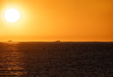 Eski Akdeniz ufkundan doğan sarı şafak güneşi turuncu bir gökyüzünün altında karides yakalamak için siluette iki balıkçı teknesini aydınlatıyor..