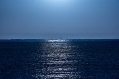 Açık, masmavi gece gökyüzü ay ışığıyla aydınlatılıyor. Işıkları Akdeniz 'in suyuna güzelce yansıyor. Ufuk çizgisinde parlak bir balıkçı teknesi var..