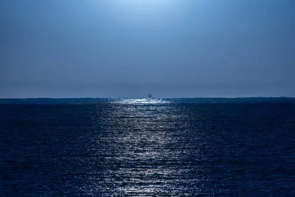Açık, masmavi gece gökyüzü ay ışığıyla aydınlatılıyor. Işıkları Akdeniz 'in suyuna güzelce yansıyor. Ufuk çizgisinde parlak bir balıkçı teknesi var..