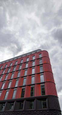 Low angle detail of the facade of the Ilona Rose House development on Charing Cross Road, London under a white sky with cobwebs of clouds backlit by the setting sun. clipart