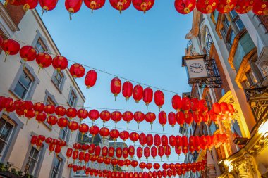 Soho 'da, Londra' nın Çin Mahallesi 'ndeki bir caddenin ön cephesinde asılı kırmızı Çin kağıt fenerlerinin gün batımı görüntüsü açık mavi bir alacakaranlık gökyüzü altında ve ön cephede asılı tipik lüks bir saat.