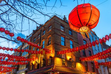 Internally illuminated Chinese New Year lantern hanging on the facade of a brick block on a street in London's Chinatown in Soho, and more lanterns in the background, under a clear blue twilight sky. clipart