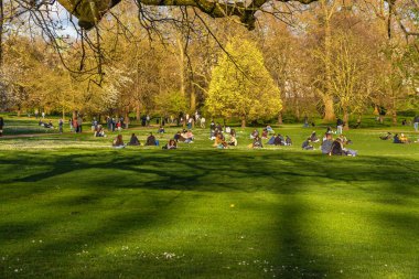 Genç öğrenciler ve arkadaşlar dinleniyor, eğleniyor, kitap okuyor ve akşam güneşinin sıcaklığıyla Londra 'daki St. James' s Park 'ın yeşil çimlerinde uzanıyor..