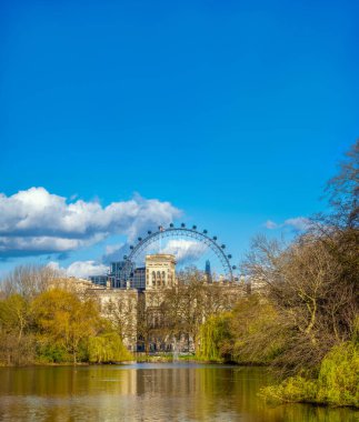 Arka planda Londra Dönme dolabı olan St James 's Park' taki gölün panoramik manzarası, Çömlek gökdelen ve akşam güneşinin aydınlattığı Viktorya dönemi binaları..