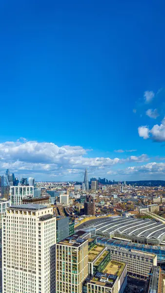 stock image Aerial view of famous London office buildings and skyscrapers of the financial district, and London train station under a sunny blue sky with low clouds on the city skyline.