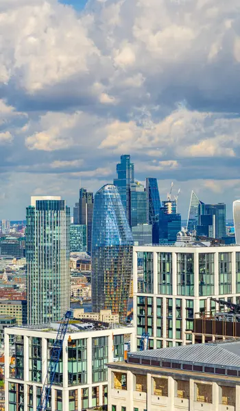 stock image Aerial view of famous London office buildings and skyscrapers from the financial district, with cranes working on new city buildings, under a sky with clouds illuminated by the evening sun.