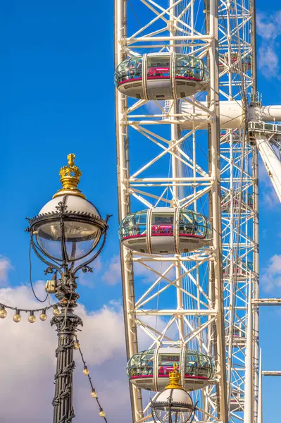 Londra Göz ya da Milenyum Göz, dünyanın en büyük ve en uzun dönme dolabı, gondolda fotoğraf çeken turistler ve aşağıda süslü bir sokak lambası var..