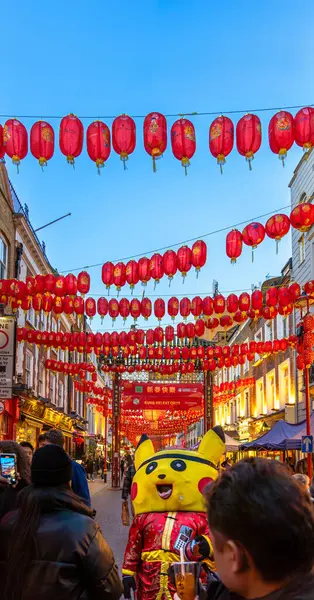 stock image Red Chinese paper lanterns hang on the facades of a street in London's Chinatown under a clear blue twilight sky with a person dressed as Pikachu and tourists taking photos.