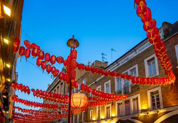 stock image Night view of red Chinese paper lanterns hanging on the facades of a street in London's Chinatown in Soho under a clear blue twilight sky.