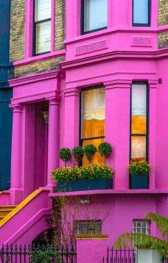 İngiltere 'nin Notting Hill kentindeki efsanevi Lancaster Yolu caddesinde mimari detayları, saksıları, saksıları ve geniş dikey pencereleri olan tipik bir İngiliz evinin pembe cephesi..