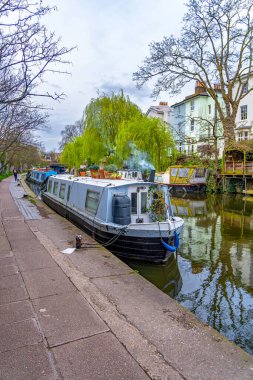 Londra 'nın Küçük Venedik' indeki Regent Kanalı boyunca koşan bir kadın. Renkli dar yüzen tekneleri Maida Vale yerleşim bölgesindeki nehre yanaşmış ve demirlemiş..