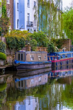 Tipik Viktorya dönemi İngiliz evlerinin aşağısındaki gezinti güvertesinde Maida Vale yerleşim bölgesine demir atmış iki mavi ve kahverengi dar kayık veya yüzen ev..