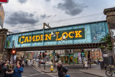 Camden High Caddesi 'ndeki efsanevi Camden Lock demiryolu köprüsü altında yürüyen insanlar ve turistler Camden Town, Londra' daki Regent Kanalı 'nı geçiyor..