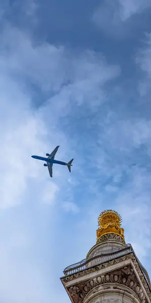 stock image Passenger plane flying through a blue sky passing by the historic column of the Monument to the Great Fire of London.