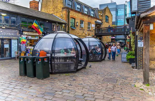 İnsanlar ve arkadaşlar Camden Market 'in içindeki yemek bölmelerinde kahve ve bira içiyorlar tarihi binalar, turistler ve ailelerle birlikte etrafta dolaşıyorlar..