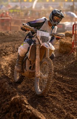 Motokros motosiklet sürücüsü bir motokros pistini çok hızlı dönüyor, ıslak ve çamurlu araziye çamur sıçrıyor dayanıklılık yarışında..