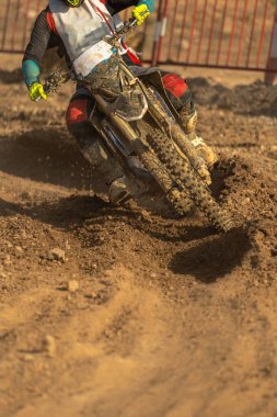 Motokros motosikletini dar bir viraja sıkıştıran bir motosiklet sürücüsü, dışarıda bir motokros ve enduro pistinde akşam güneşiyle aydınlatılan ıslak toprak bir pistte..