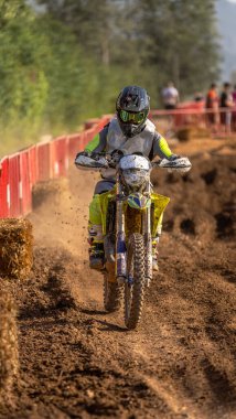 Bir off-road yarışı sırasında siyah kasklı motokros sürücüsü arka tekerlekten çakıl fırlatıyor..