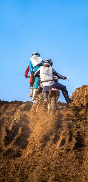 stock image Motocross riders controlling their bikes as they climb a mud and gravel hill to the top with their wheels throwing mud and dirt off their knobby rear tires during an off-road endurance competition under a clear blue sky.