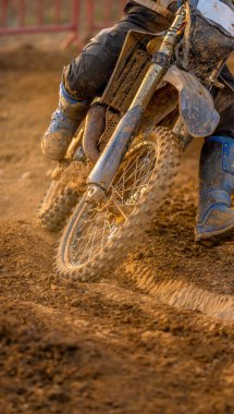 Çamurlu bir arazide çamurlu bir virajda giden bir off-road motosikletinin ayrıntıları ve çamurla kirlenmiş binicinin botları..