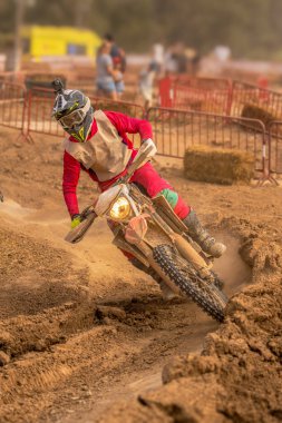 Motokros binicisi kaskında kamera ile motosikletini katlarken son sürat çamurlu yolda giderken keskin bir dönüş yaparak arka tekerleğinden toz ve çakıl fırlatıyor..