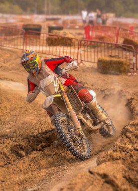 Motokros sürücüsü motorsikletini döndürüyor ve katlıyor. Çamurlu bir pistte son sürat giderken keskin bir viraj alıyor. Arka tekerinden ve arkadaki seyircilerden toz ve çakıl fırlatıyor..