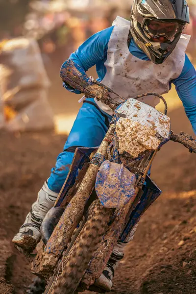 Mavi tulumlu motokros binicisi motosikletini yan yana katlayarak açık hava dayanıklılık yarışması sırasında ıslak çamurlu arazide keskin bir dönüş yapıyor..