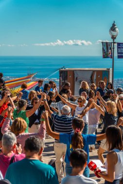 Bir grup son sınıf öğrencisi Barcelona 'da güneşli bir günde Akdeniz arkasındayken geleneksel Katalan sardanasıyla el ele tutuşarak dans ediyor..