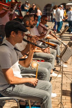 Group of musicians from a Catalan cobla playing wind instruments and sardana songs in an open-air performance with people dancing the sardana dance in the background. clipart