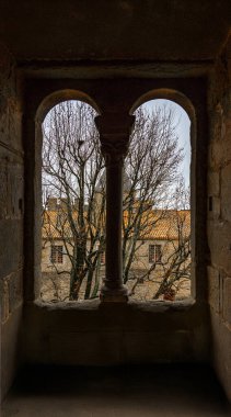 View of the medieval architecture of Carcassonne through a window with two stone arches on a cloudy day. clipart