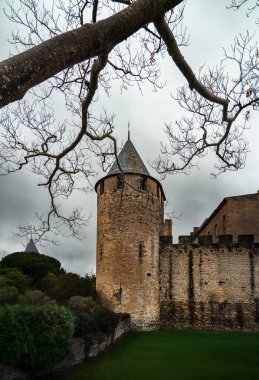 Watchtower of the Comtal Castle of Carcassonne through the bare branches of a tree under a cloudy sky. clipart