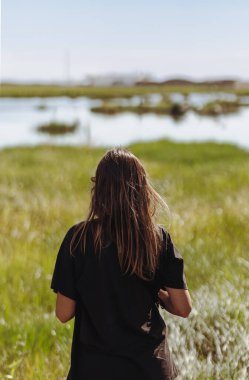 Young woman, with her back turned, in the Ebro Delta, looking at the serene landscape of the wetlands on a sunny day. clipart