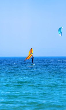 Kanat Foil atleti, Tarifa, İspanya sahillerinde hız kazanmak için kollarıyla turuncu bir yelkenli tutuyor..