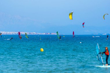 Birkaç rüzgar sörfçüsü, uçurtmacılar ve kanat folyoları arka planda Tarifa kıyısı ve şehriyle güneşli bir günün tadını çıkarıyorlar..