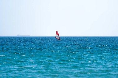 Rüzgâr sörfçüsü bulutlu bir gökyüzü ve ufukta bir kargo gemisiyle Tarifa, İspanya 'da mavi denizin üzerinde süzülüyor..
