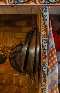 Tuğla duvarda eski demir tavalar ve paella tavaları asılı, taşralı bir mutfak..