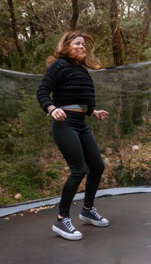 Bacakları bükülmüş genç bir kadın ormanda trambolinde zıplamaya başlıyor..