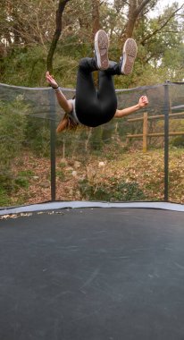 Ormandaki bir parkta trambolinde ters takla atan genç bir kadın..