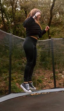Genç, sportif bir kadın, doğal bir parktaki trambolinde mutlu bir şekilde zıplamaktan zevk alıyor..